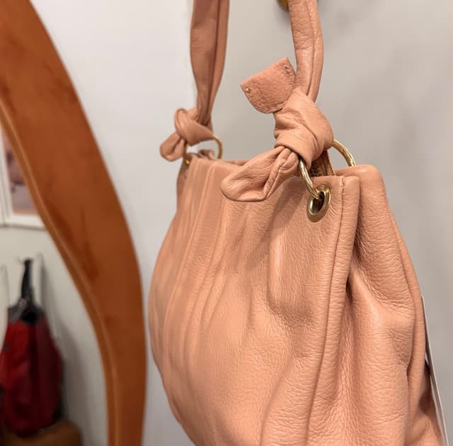 Bolsa Jorge Bischoff rosa nude pendurada na loja, mostrando o nó das alças