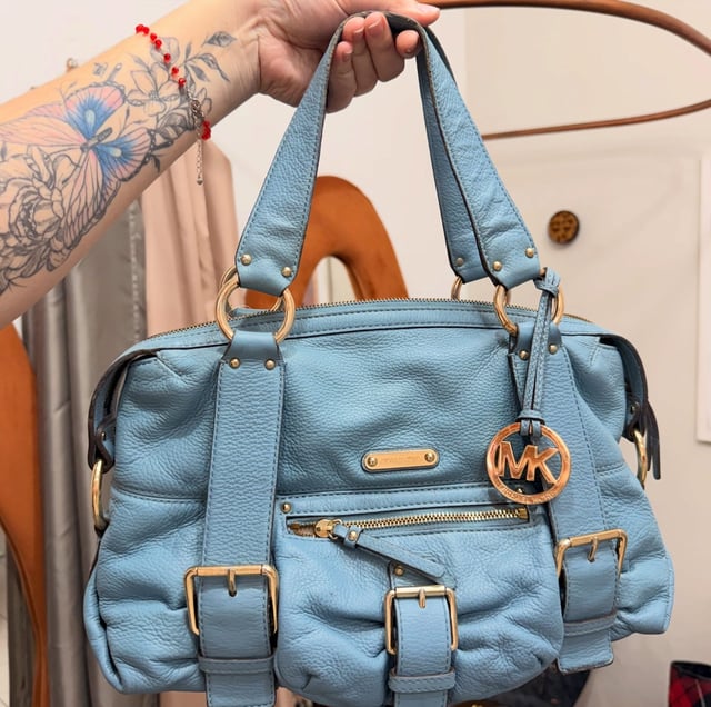 Ketlen segurando a bolsa Michael Kors azul-celeste pelas alças, na loja